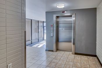 an elevator in a hallway with a tiled floor and stainless steel doors